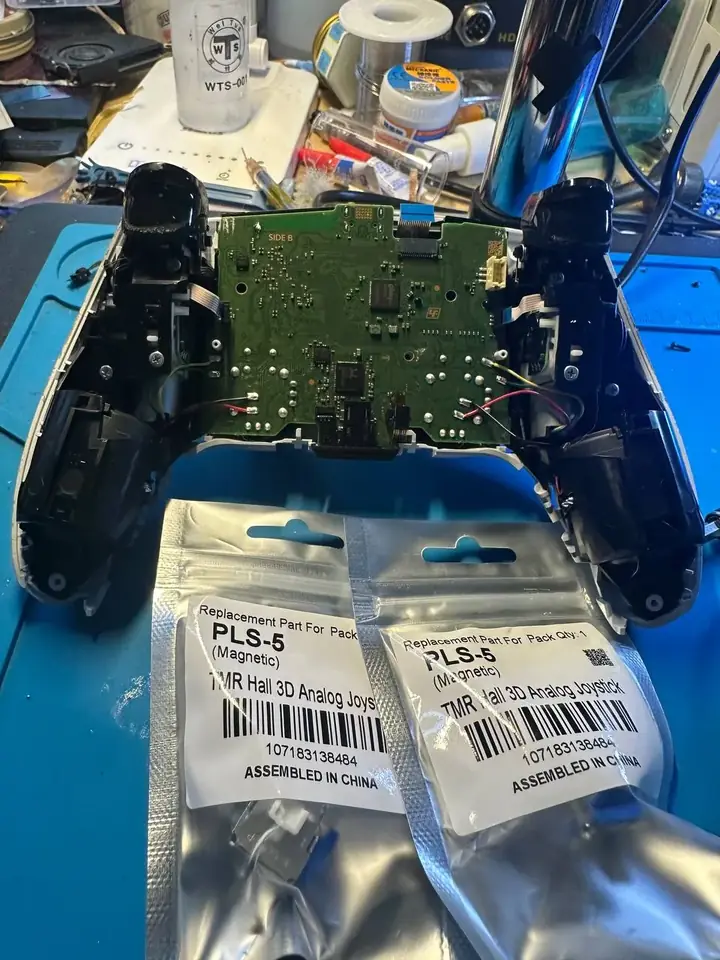 DualSense controller opened with its main board exposed and replacement joysticks ready