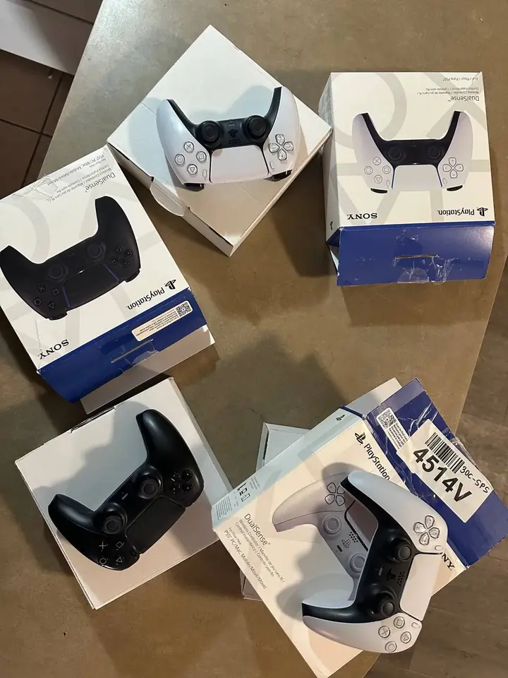 Several white and black PS5 DualSense controllers with their original boxes