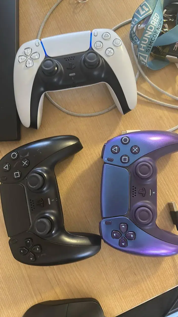 White, black and purple PS5 DualSense controllers on a desk
