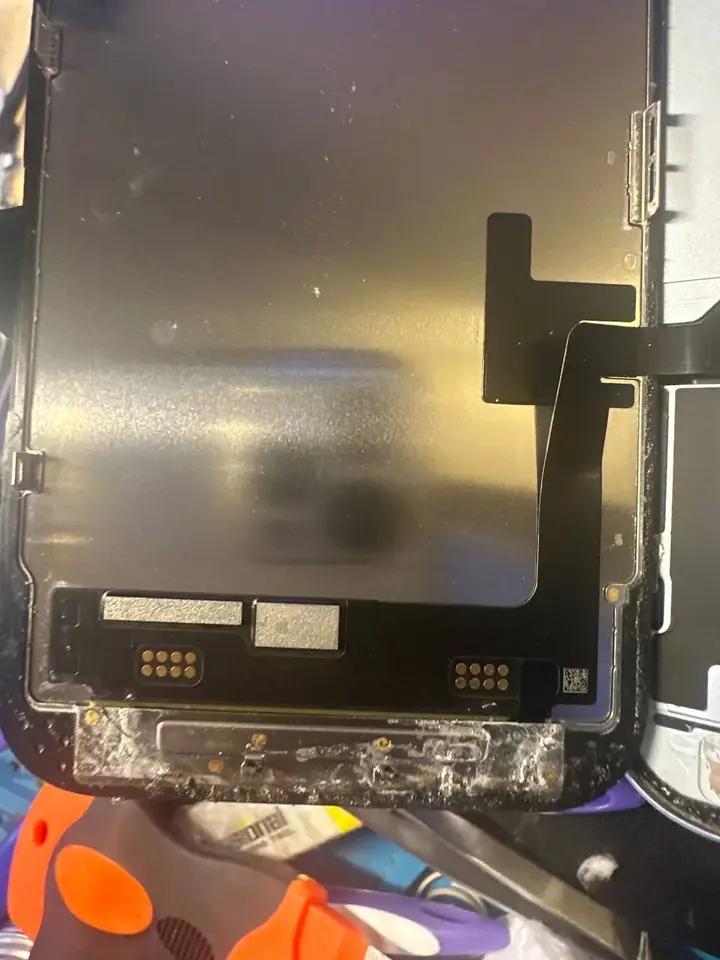 Underside of an iPhone display showing the flex connector and old adhesive