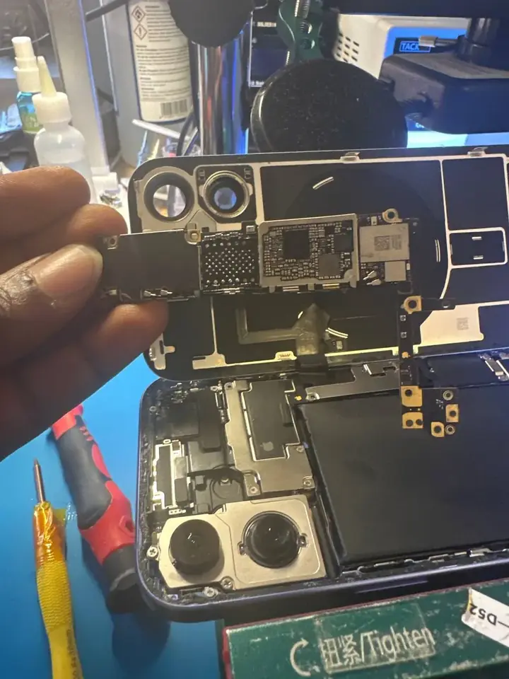 iPhone logic board removed and held above the opened phone during repair