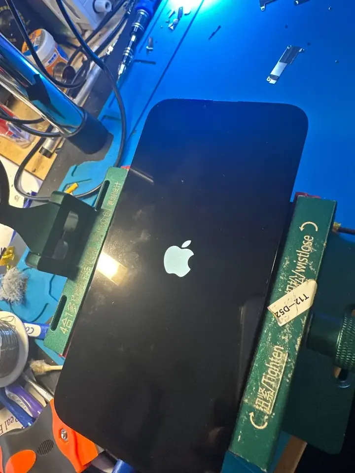 iPhone in a repair holder showing the Apple logo on its new screen during first boot