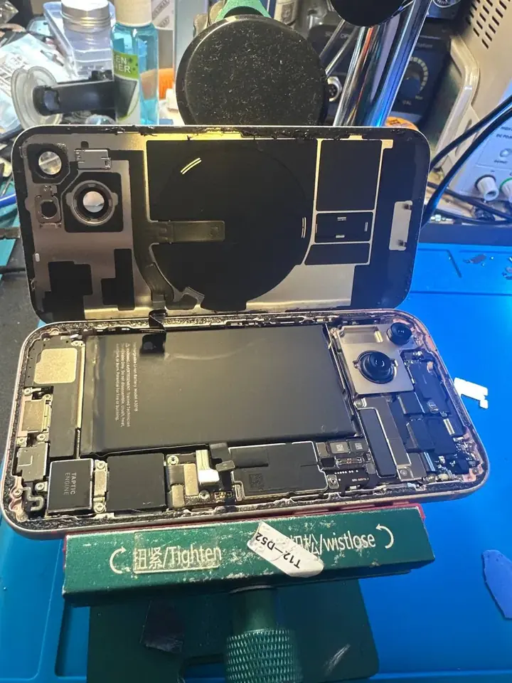 Pink iPhone opened in a repair holder with the back glass lifted for charging port replacement