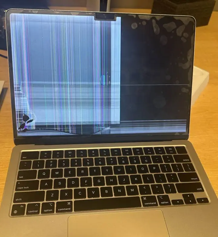 Laptop with a damaged display showing vertical lines and a cracked lower corner