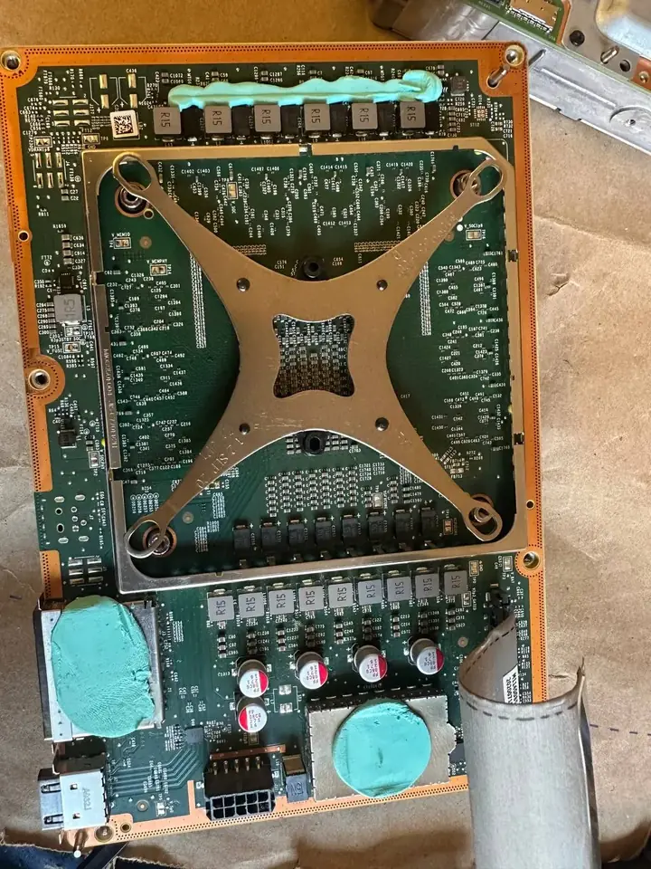 Rear of an Xbox Series X motherboard with the APU retention bracket and thermal putty on the power stages